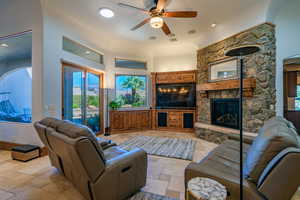 Living area featuring stone tile flooring, a ceiling fan, a fireplace, a high ceiling, and recessed lighting