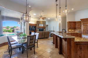 Kitchen with a ceiling fan, hanging light fixtures, stone tile floors, wood finish cabinets, and light stone counters