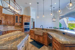 Kitchen with wood finish cabinetry, dark stone countertops, a large island with sink, and glass fronted cabinets
