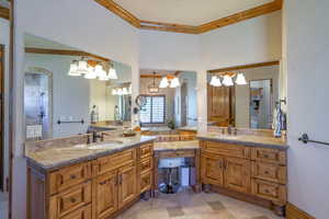 Bathroom with two vanities, ornamental molding, hanging lights, and tiled shower