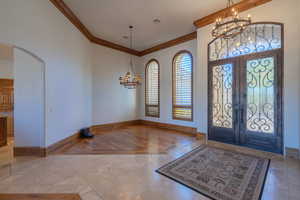 Foyer with a chandelier, arched walkways, french doors, and crown molding