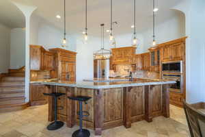 Kitchen with wood finish cabinets, decorative backsplash, light stone countertops, a kitchen breakfast bar, and stone tile flooring