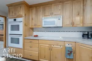 Kitchen featuring white appliances, light countertops, backsplash, and light wood finish cabinets