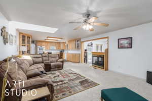 Living area featuring a fireplace, a skylight, light colored carpet, ornamental molding, and a ceiling fan