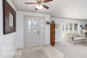 Entrance foyer with ceiling fan, ornamental molding, light carpet, and light tile patterned floors