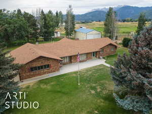 Back of house featuring a lawn, a shingled roof, a mountain view, brick siding, and a view of countryside