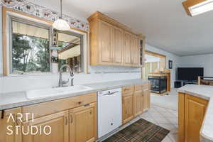 Kitchen with tasteful backsplash, white dishwasher, light countertops, and light wood finish cabinetry