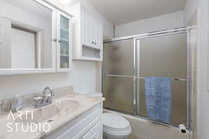 Primary bathroom featuring vanity, bath / shower combo with glass door, and a textured ceiling