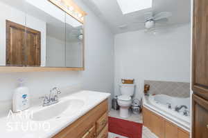 Bathroom featuring a skylight, a ceiling fan, vanity, light tile patterned floors, and a bath