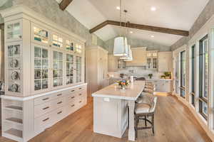 Kitchen with wallpapered walls, glass fronted cabinets, an island with sink, light wood-type flooring, and a breakfast bar