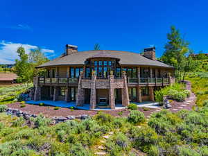 Back of property featuring a chimney, stone siding, a balcony, and a patio