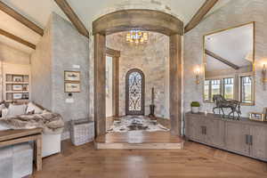 Foyer entrance with lofted ceiling with beams, suspended lighting, light wood finished floors, and arched walkways