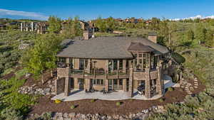Rear view of house featuring a patio, a chimney, a balcony, and view of wooded area