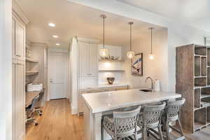 Kitchen with open shelves, a kitchen bar, a peninsula, pendant lighting, and light wood-type flooring