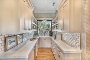 Kitchen featuring light stone counters, open shelves, decorative backsplash, light wood-type flooring, and decorative light fixtures