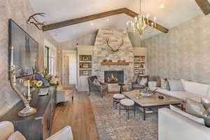 Living room with wallpapered walls, light wood-style floors, a stone fireplace, and hanging lights