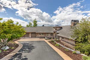 View of front of house featuring stone siding, driveway, a garage, a chimney, and a shingled roof