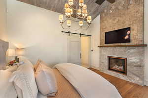 Bedroom with a barn door, wood finished floors, a fireplace, hanging lights, and a vaulted wood ceiling