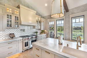 Kitchen featuring glass insert cabinets, range with two ovens, light stone countertops, wallpapered walls, and light wood-style flooring