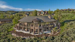 Rear view of property with stone siding, a chimney, a balcony, a patio area, and view of wooded area