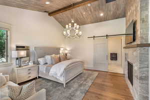Bedroom featuring a barn door, a chandelier, hardwood / wood-style flooring, a fireplace, and a high wood beamed ceiling