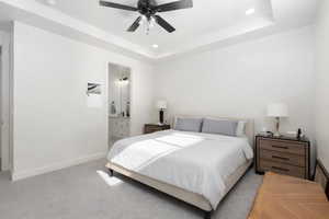 Bedroom featuring a raised ceiling, recessed lighting, connected bathroom, a ceiling fan, and light carpet