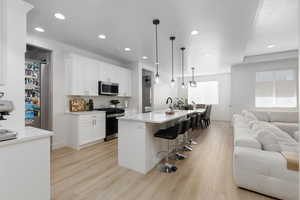 Kitchen featuring open floor plan, a kitchen bar, a kitchen island with sink, light wood-type flooring, and stainless steel appliances