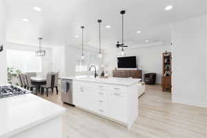 Kitchen with light wood-style flooring, open floor plan, a kitchen island with sink, a ceiling fan, and light stone counters