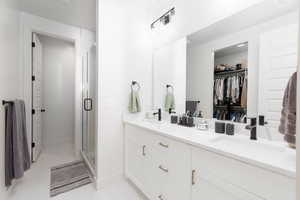 Bathroom with double vanity, a spacious closet, and a stall shower