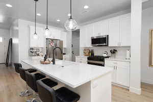 Kitchen with a breakfast bar area, a kitchen island with sink, stainless steel appliances, and white cabinets