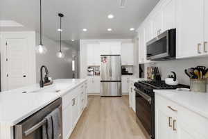 Kitchen with stainless steel appliances, white cabinets, light wood-style flooring, pendant lighting, and light stone counters