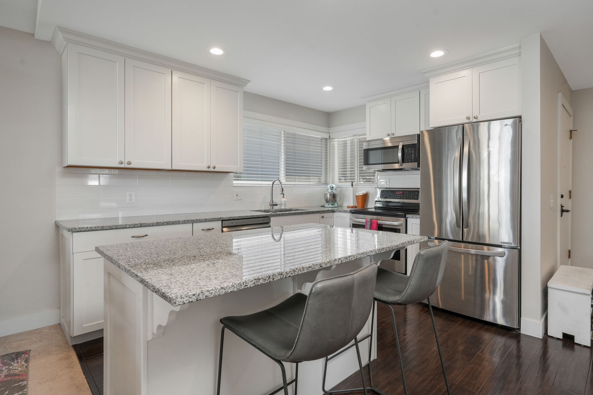 Kitchen featuring light stone counters, a breakfast bar area, stainless steel dishwasher, backsplash, and white cabinets