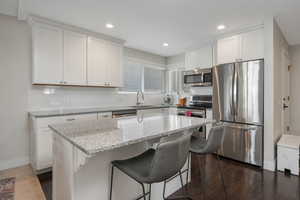Kitchen featuring light stone counters, a breakfast bar area, stainless steel dishwasher, backsplash, and white cabinets