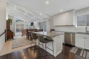 Kitchen featuring stainless steel appliances, white cabinets, a kitchen bar, light stone counters, and a center island
