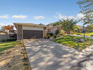 Ranch-style house with an attached garage, driveway, roof with shingles, brick siding, and a front lawn