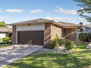 Ranch-style house with an attached garage, driveway, roof with shingles, brick siding, and a front lawn