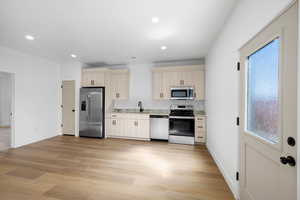 Kitchen with stainless steel appliances, light wood-style flooring, recessed lighting, and light stone counters