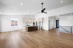 Dual tone kitchen with open floor plan, a center island with sink, light countertops, stainless steel appliances, and light wood finished floors