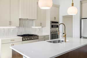Kitchen featuring backsplash, light stone countertops, stainless steel appliances, hanging light fixtures, and an island with sink