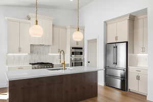 Two tone kitchen featuring stainless steel appliances, an island with sink, dark wood-type flooring, decorative light fixtures, and lofted ceiling