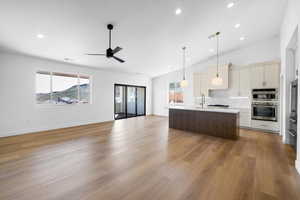 Dual tone kitchen featuring open floor plan, a kitchen island with sink, vaulted ceiling, light wood finished floors, and ceiling fan