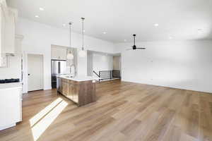 Kitchen featuring an island with sink, open floor plan, decorative light fixtures, a high ceiling, and light wood-style flooring