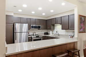 Kitchen featuring stainless steel appliances, a peninsula, light stone counters, tasteful backsplash, and recessed lighting