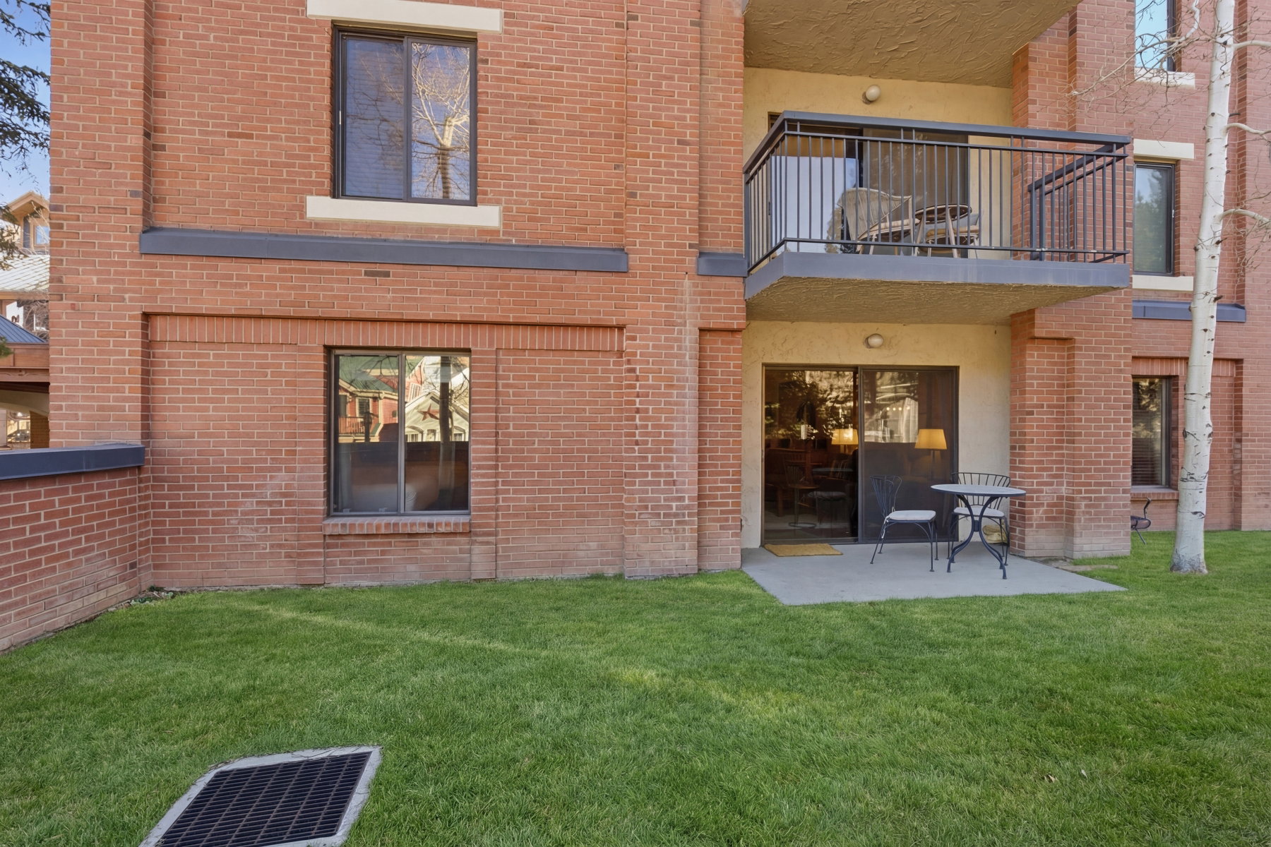 Rear view of property featuring a balcony, brick siding, a patio area, and a yard