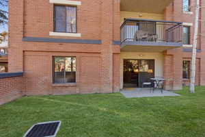 Rear view of property featuring a balcony, brick siding, a patio area, and a yard