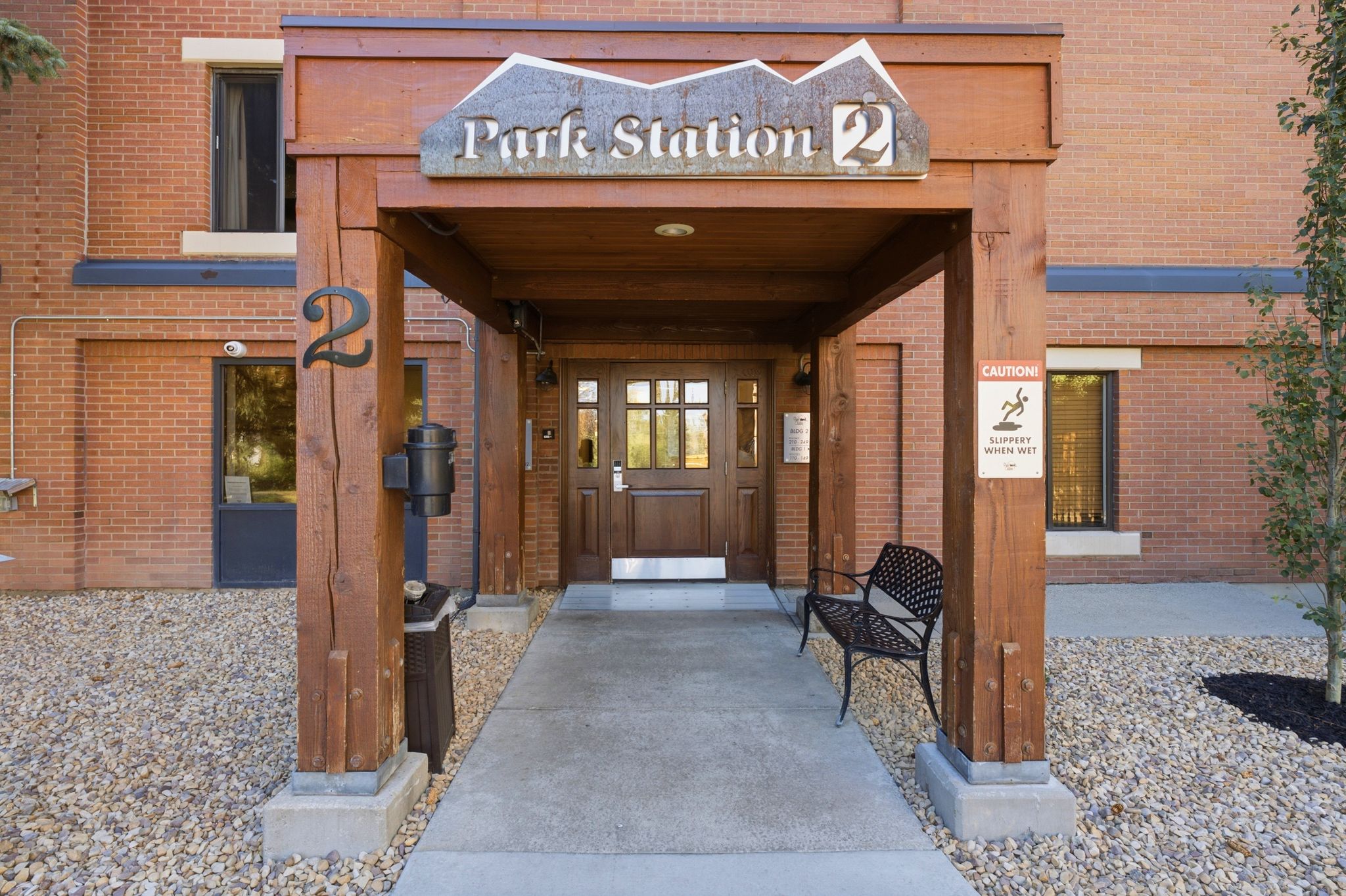 Welcoming building entrance featuring a robust timber frame portico, a solid wood door with glass inserts, and a concrete walkway