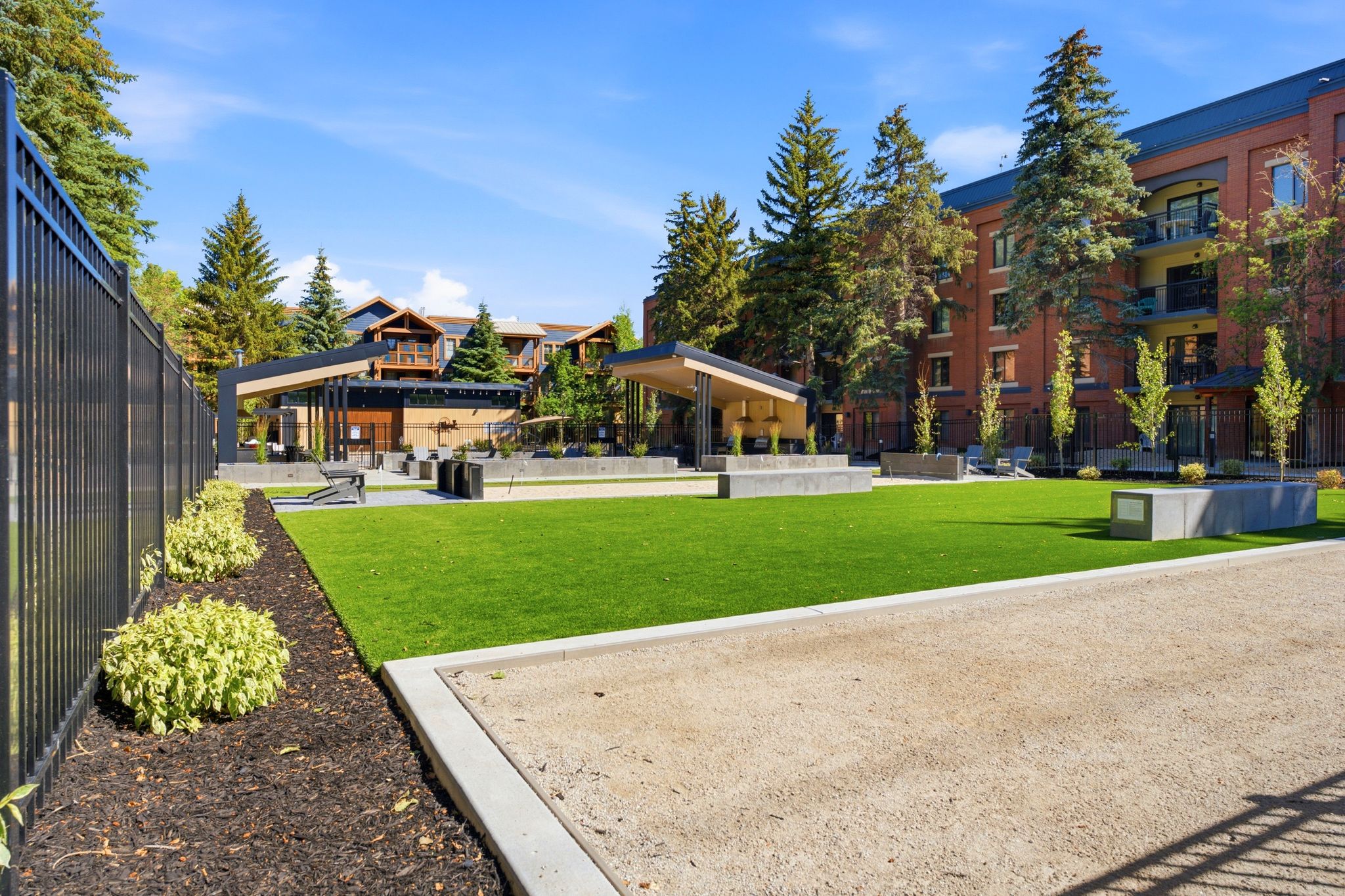 Community green space featuring a manicured lawn, gravel recreation area, and mature evergreen trees
