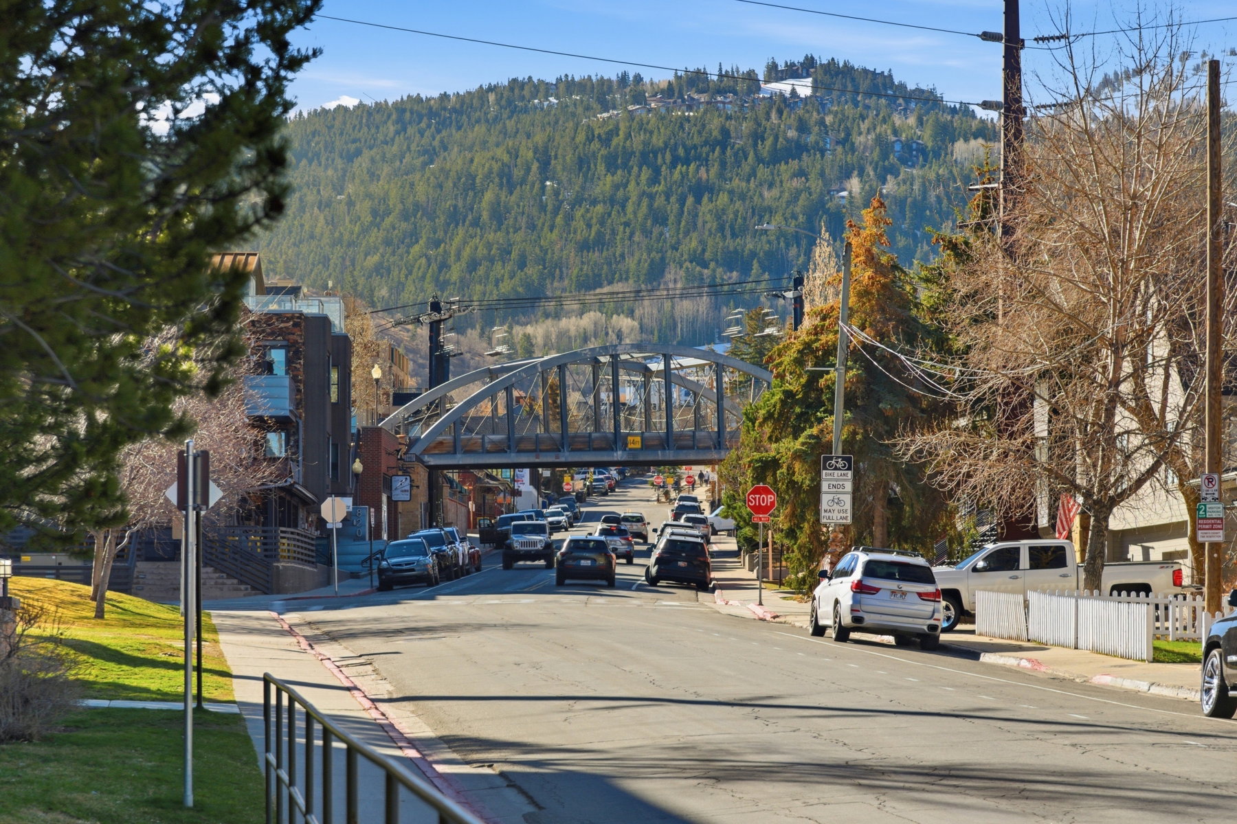 View of asphalt street with traffic signs, a wooded view, sidewalks, and curbs