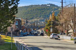 View of asphalt street with traffic signs, a wooded view, sidewalks, and curbs