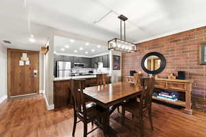 Dining area with dark wood-style floors, brick wall, and suspended lighting